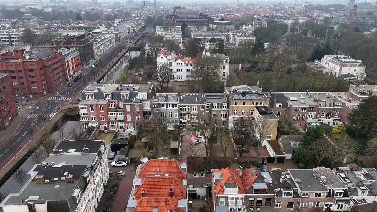 Dutch settlement with townhouses and homes near canal in suburb neighborhood. Aerial lateral wide shot. The Hague city with bike lane and leafless trees in winter.
