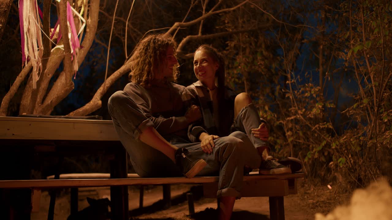 사랑에 빠진 한 부부는 불 근처의 나무 벤치에 앉아서 이야기하고 있습니다. 도시 밖의 파티. 시골 집에서 휴식을 취합니다.