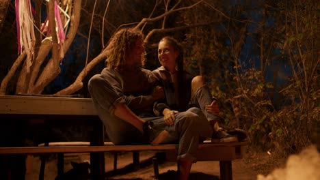 a couple in love is sitting on a wooden bench near a fire and talking. party outside the city. rest in the country house
