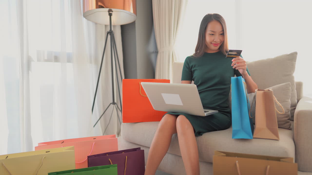 거실에서 편안하게 노트북을 사용하여 신용 카드나 직불 카드로 온라인 쇼핑을 하는 젊은 여성