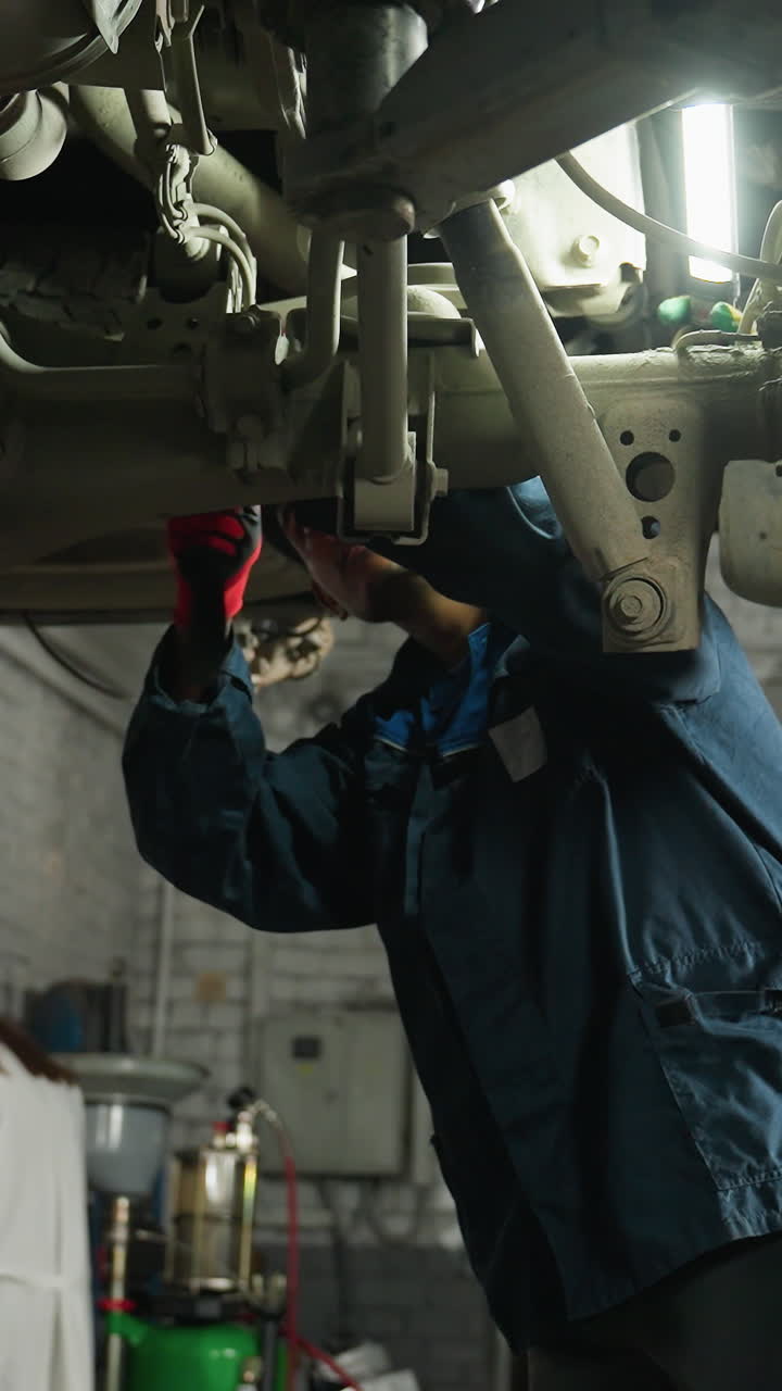 ingeniero de automóviles sostiene la luz mientras ayuda a un colega que trabaja debajo del vehículo, ajustando la posición de la mano para señalar algo específico en el mecanismo del automóvil