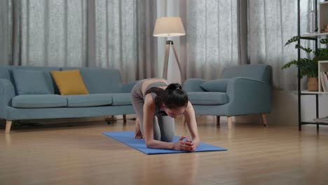 vista completa de joven entrenadora asiática mujer en ropa deportiva hablando y haciendo yoga en la postura de tabla del antebrazo mientras enseña ejercicios en casa