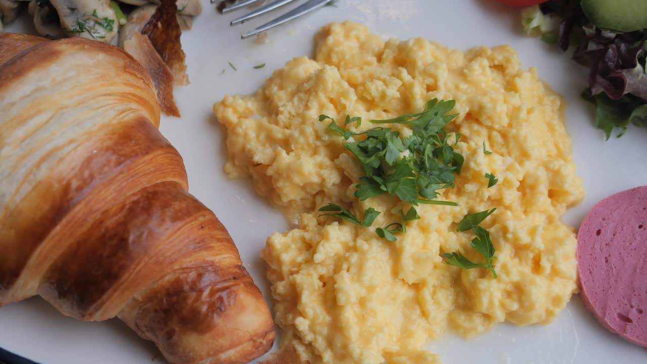 Breakfast Plate with Scrambled Eggs, Croissant, Sausage, and Salad