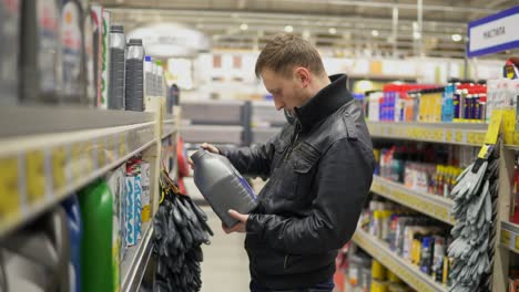 young man is choosing motor oil for car at repair service station or in supermarket. he looks on a few canisters, chooses one and goes to pay for it. different canisters on shelves