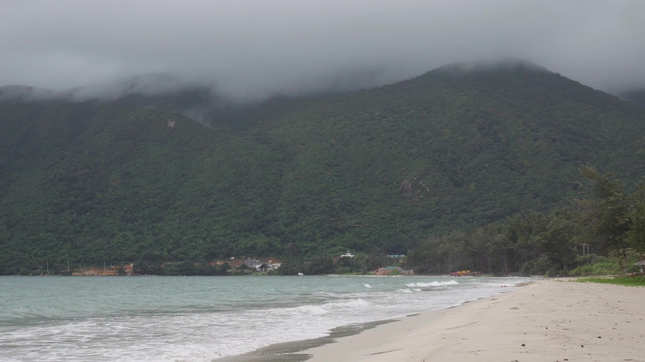 Zalesněné hory u tropické pláže během mlžného rána na ostrově Con Dao, Vietnam. Široký záběr