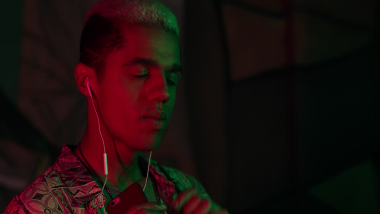 vista de cerca de un joven afroamericano con estilo escuchando música con auriculares y bailando enérgicamente al aire libre por la noche
