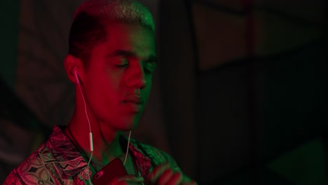 close-up view of young african american stylish man listening music in headphones and dancing energetically outdoors at night