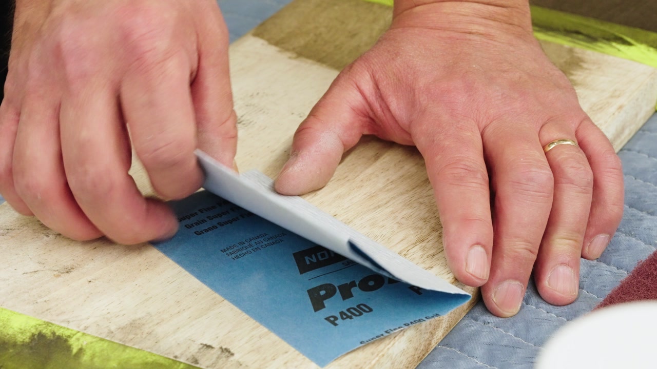 Blue sandpaper smooths wooden plank in close-up inside a woodworking shop