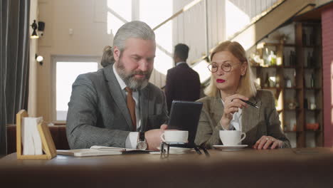 senior colleagues using tablet and speaking in cafe