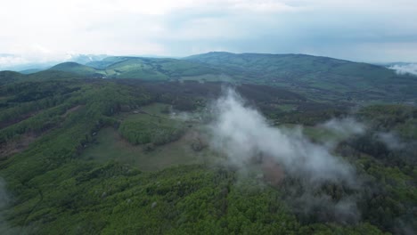 single-cloud-floating-in-the-air-above-a-green-mountain-forest-area,-nature-aerial-drone-shot,-vegetated-mountains,-foggy-rainy-weather-in-Banska-Bystrica,-Tatra-Mountains-forest,-Slovakia