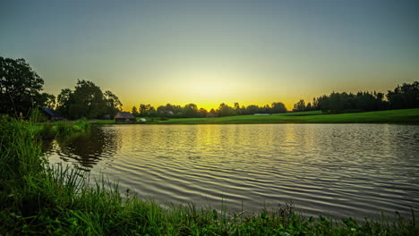 Glowing-sunrise-over-lake-homestead-in-rural-Latvia,-time-lapse-view