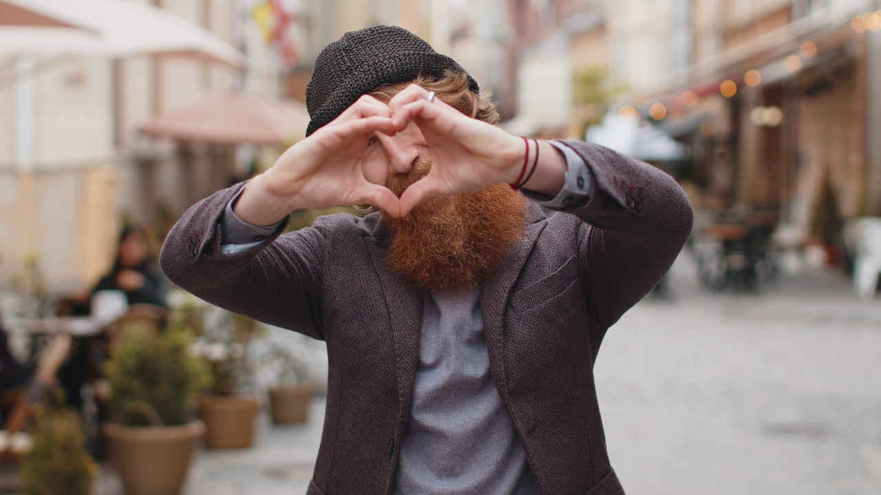 Bearded man makes symbol of love showing heart sign to camera express romantic positive feelings