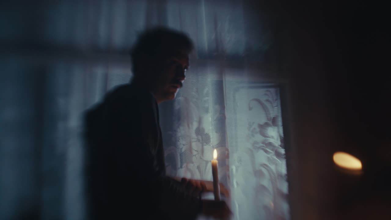 Silhouette of a person with a lit candle by a window at night