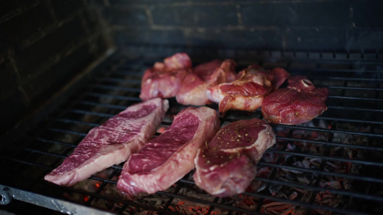 Pezzi assortiti di carne cruda posizionati su una griglia sopra carboni ardenti prima della cottura.