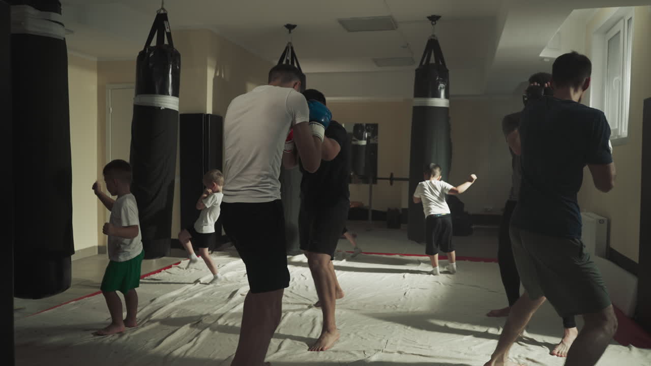 Children and adults exercise in martial arts club. Kick-boxers do combat exercises with punching equipment in fighting gym slow motion. Battle techniques