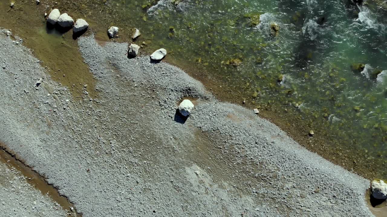 일출에 자갈과 절벽이 빛나는 강둑, 겨울에 태양 광선을 반사하는 맑은 물, 공중 하향식 전망