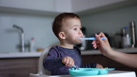 mother feeding her son from spoon. mom uses napkin to clean kid's mouth while child hits a plate with his fork.