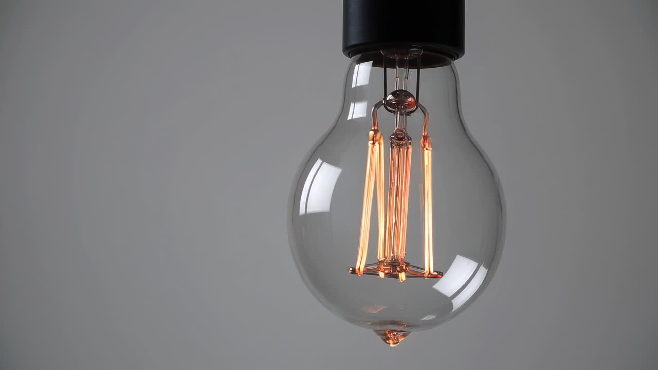 Close-up video of a hanging light bulb against a gray background, captured from a low angle