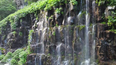 Una-Fascinante-Cascada-Que-Cae-Por-Acantilados-Rocosos,-Rodeada-De-Una-Exuberante-Vegetación-Verde