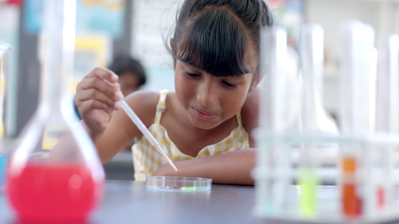 In a school classroom setting, a young biracial girl is focused on a science experiment