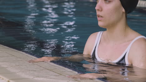 primer plano de una joven nadadora descansando en el borde de la piscina cubierta después de una sesión intensiva de natación