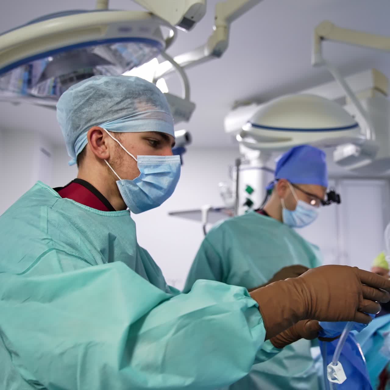 Main surgeon passes surgery device to his assistant. Doctor inserts tube into patient at backdrop. Other assistants at background