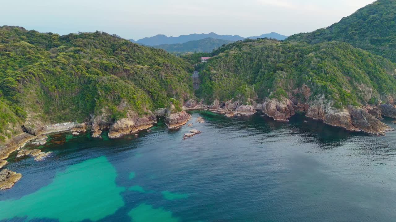 A breathtaking aerial shot flying over a secluded bay. The crystal-clear turquoise water meets lush green cliffs, creating a stunning, untouched paradise perfect for travel and nature themes