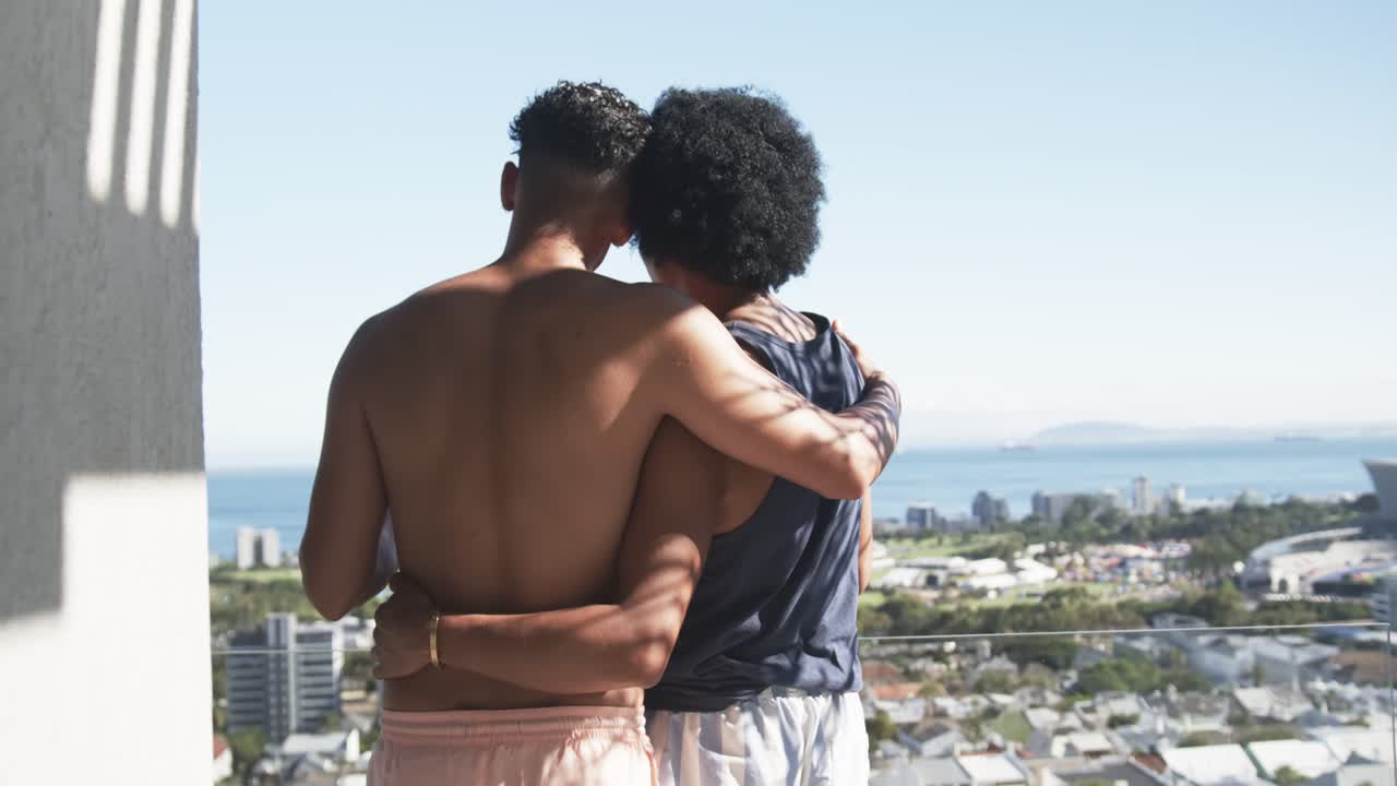 Uomini afroamericani a torso nudo che si appoggiano con un braccio sulla spalla, guardando l'oceano dal balcone.