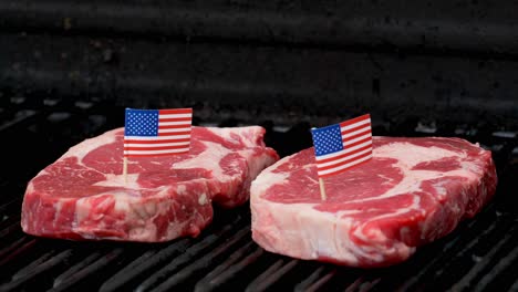 Two-juicy-rib-eye-steaks-sitting-on-the-grill-and-cooking-with-two-tiny-American-flags-tooth-picked-into-them