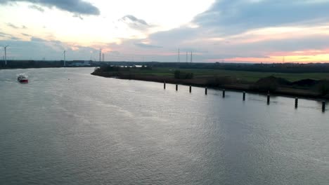 windmills on the side of a river with a cargo freight on an overcast day