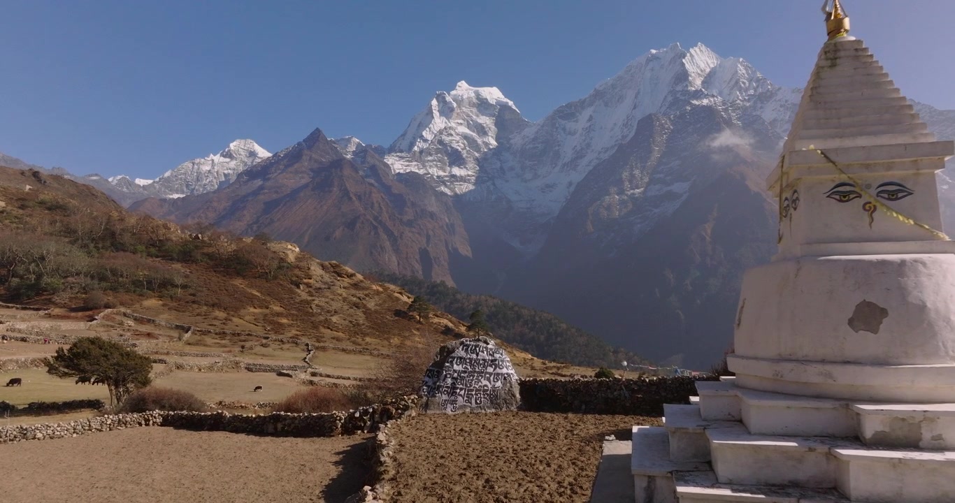 Phortse village, Everest, Nepal, aerial push-in shot of a traditional white Buddhist stupa with the Buddha's eyes painted on it, with Ama Dablam mountain peak rising behind agricultural fields