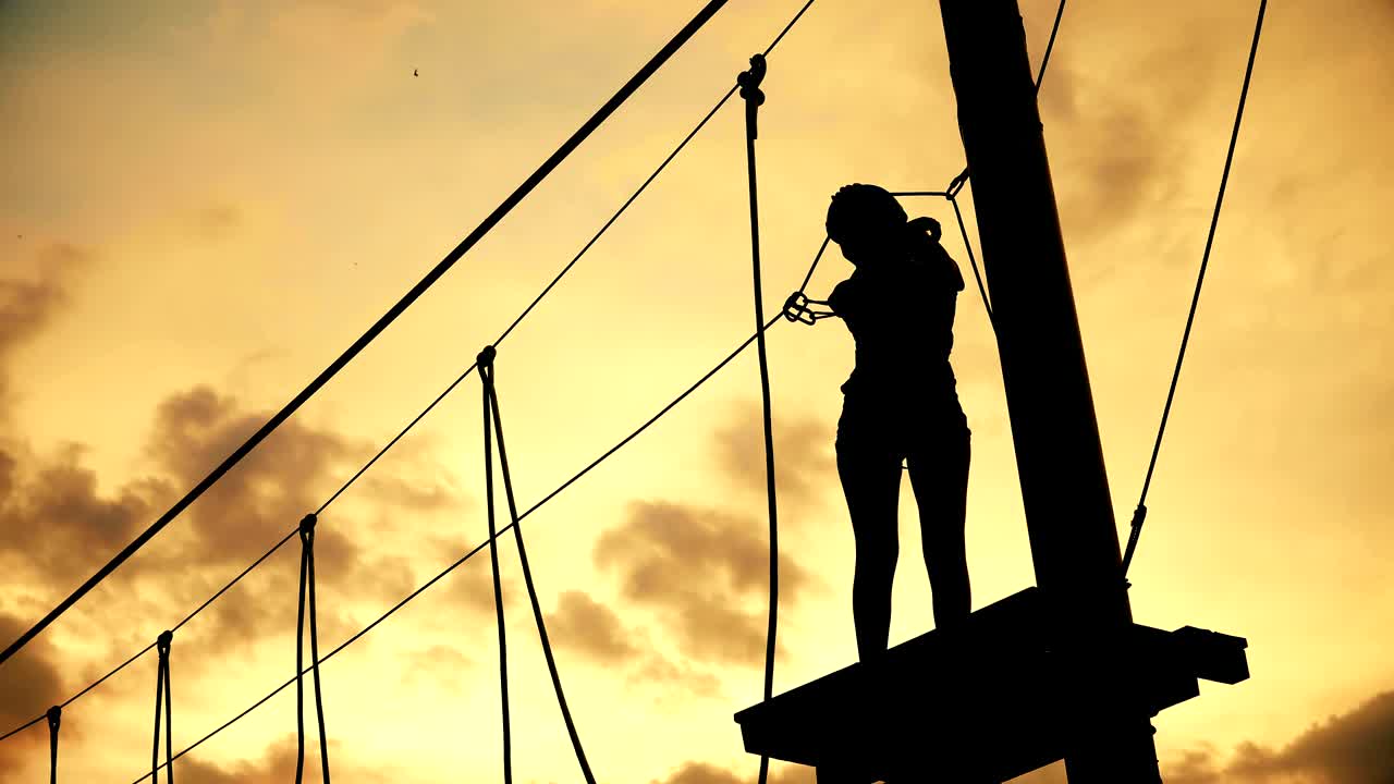 Silhouette girl celebrate adventure park finish with hands wide open and dancing at sunset