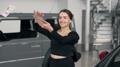 mujer joven feliz esparciendo dinero en un concesionario de automóviles