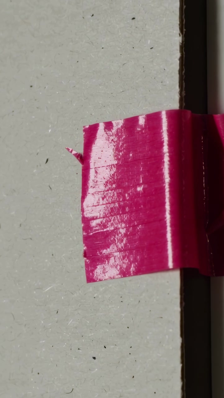 Vertical video: Camera moving closer, pink tape highlighting gloss and torn tab at seam, copy space