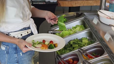 mujer que se sirve ensalada en un buffet