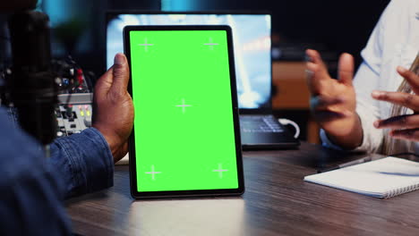 tableta de pantalla verde sostenida por vlogger anfitrión del programa charlando con el invitado en luces de neón estudio adornado