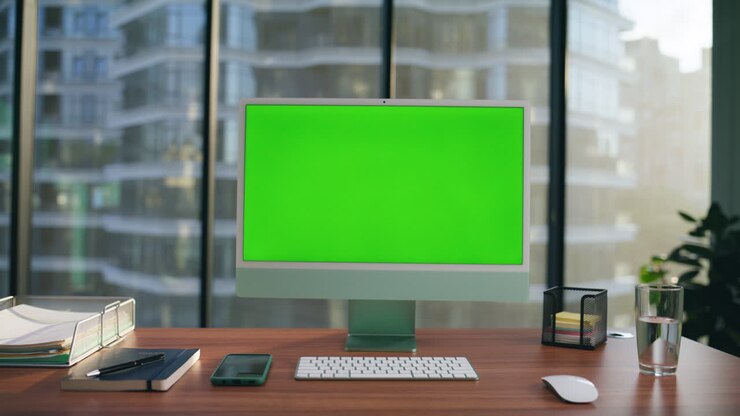 Monitor di computer mockup posizionato sulla scrivania in primo piano. PC con schermo verde in un ambiente di lavoro moderno.