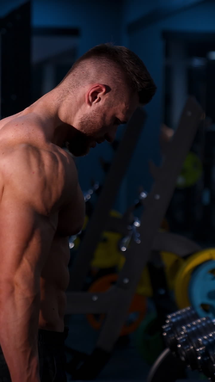 Muscular Bodybuilder Man Holding Dumbbells. Fit young man holding dumbbells while working out at gym. Vertical video
