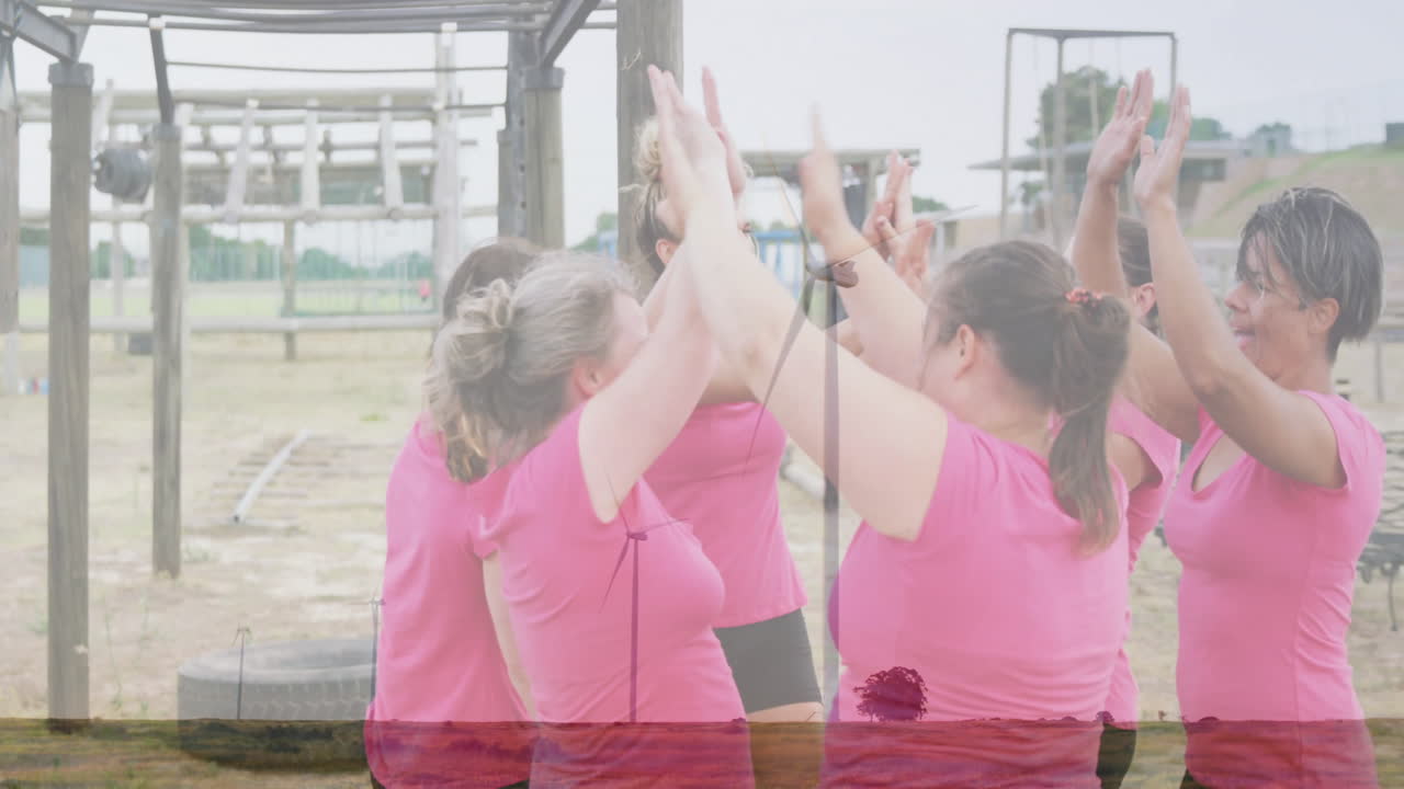 Celebrating with high fives, women in pink shirts at outdoor obstacle course