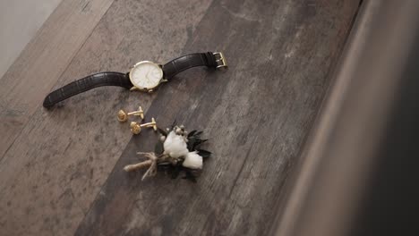 reloj de pulsera de oro, gemelos y botones elegantemente exhibidos en una superficie de madera rústica