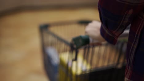 las manos femeninas llevan un carro en el supermercado a través de los pasillos