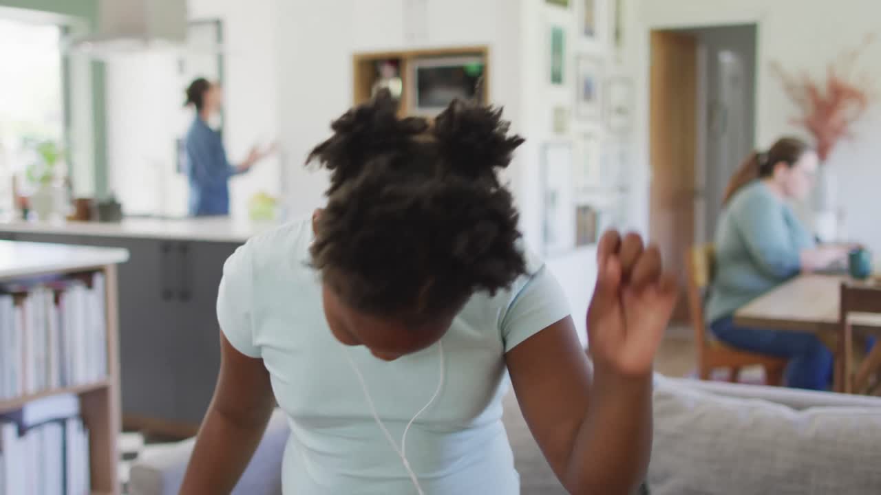 Happy african american girl wearing earphones and dancing in living room