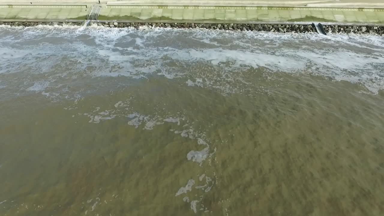 Drone shot of the coastline, flying backwards while looking at sea defences and then the ocean. Providing an aerial view of the coastal defences protecting the land