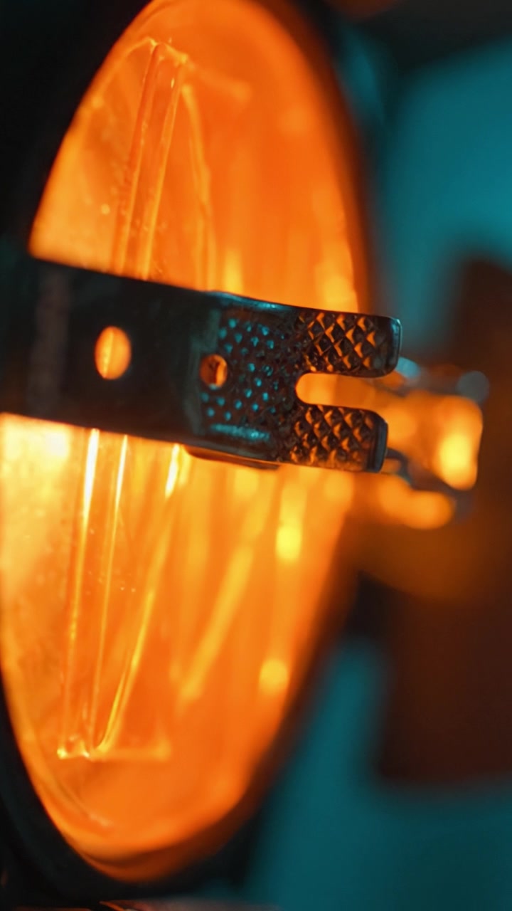 Primo piano di un componente di lampada illuminato con un caldo bagliore arancione e una staffa testurizzata a fuoco, che mostra effetti di luce e dettagli unici.