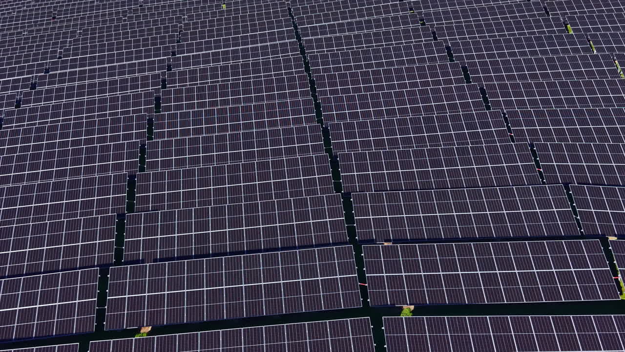 File di pannelli solari catturano la luce del sole in un'ampia distesa durante il giorno, vicino a un'area rurale incentrata sull'energia rinnovabile.