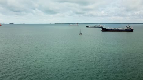 Small-Sailboat-sails-in-the-Indian-Ocean-close-to-Malaysia-between-Many-Large-Cargo-Ships