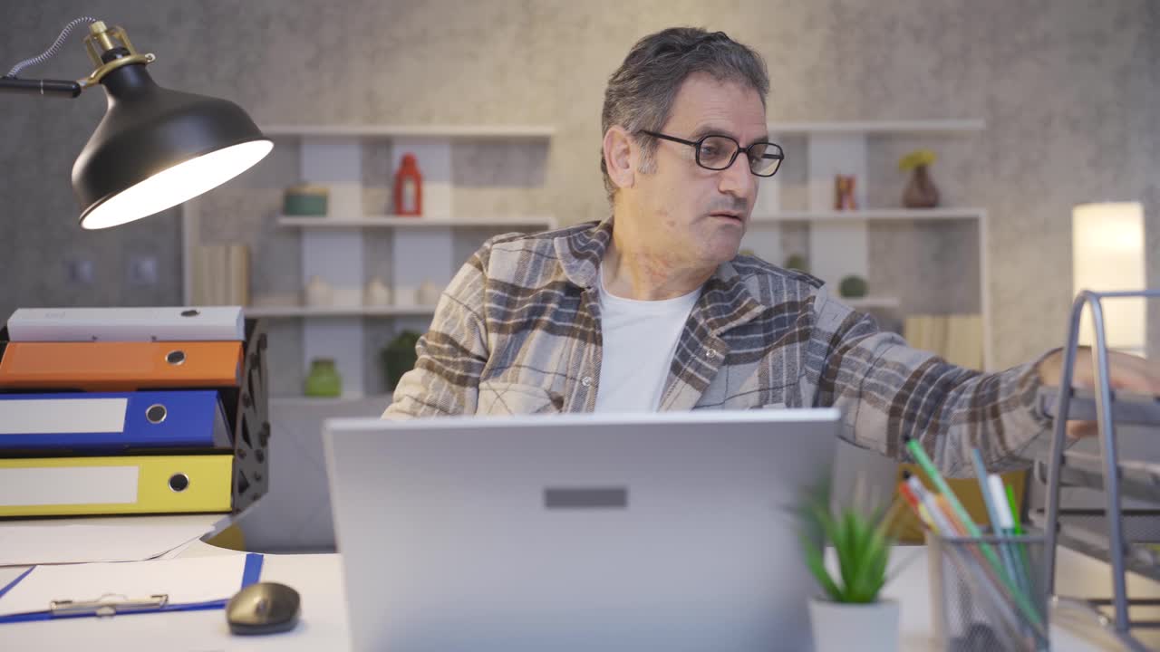 A mature man who works intensely and quickly in his home office.