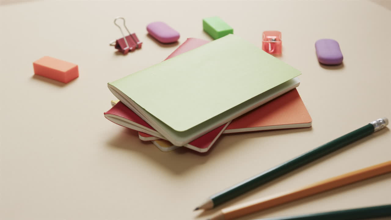Close up of colourful notebooks with school stationery on beige background, in slow motion