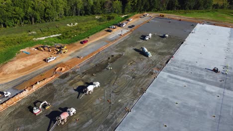 Two-workers-walk-at-a-construction-site-past-several-large-concrete-trucks