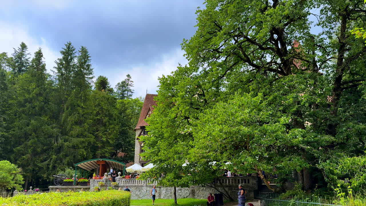 Beautiful lush greenery hiding the old castle. Lots of people walk by the location. Pele? Castle in the Carpathian Mountains, Romania
